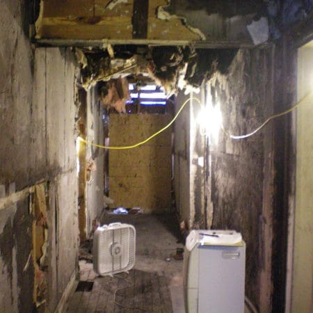 A hallway featuring a refrigerator on one side and a door at the end, with neutral-colored walls and flooring.